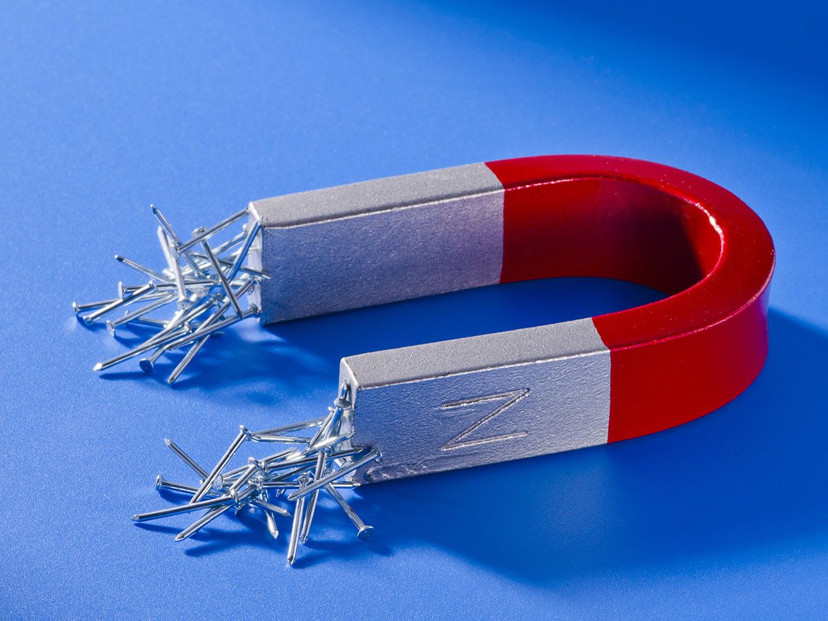 Red and chrome magnet with small nails sticking to the ends sitting on a blue surface