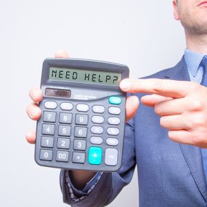 White man in business suit holding a calculator that says “Need Help?”
